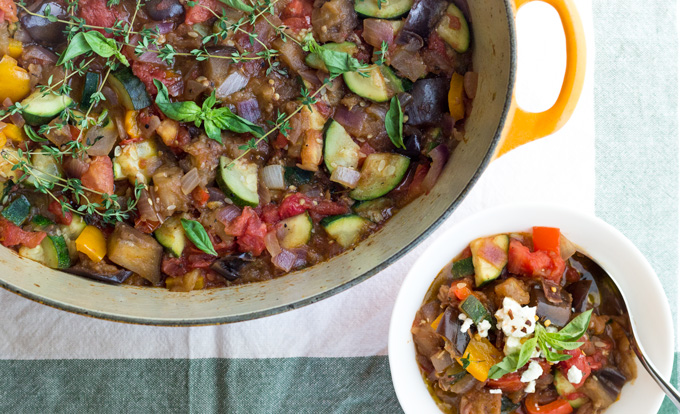 Cropped view of a rustic stew in a large dutch oven pan alongside a bowl serving of the rustic stew with a spoon