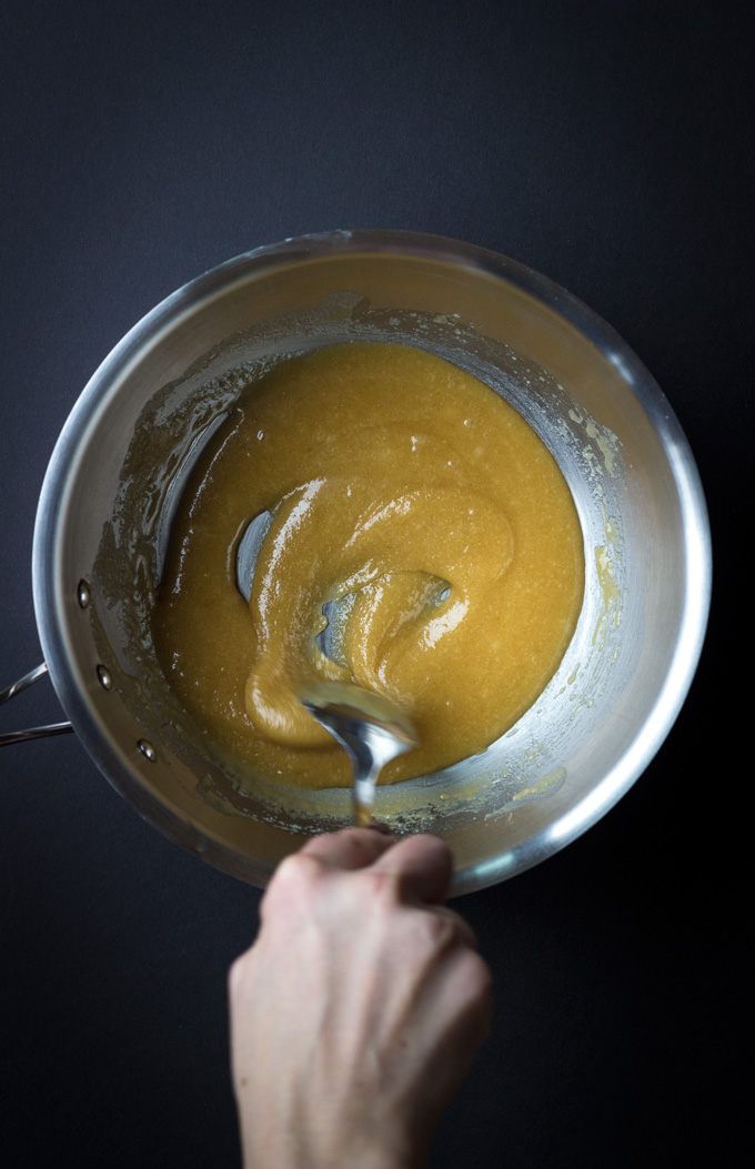 Silver mixing bowl of caramel with hand stirring mixture with a black backgrounf